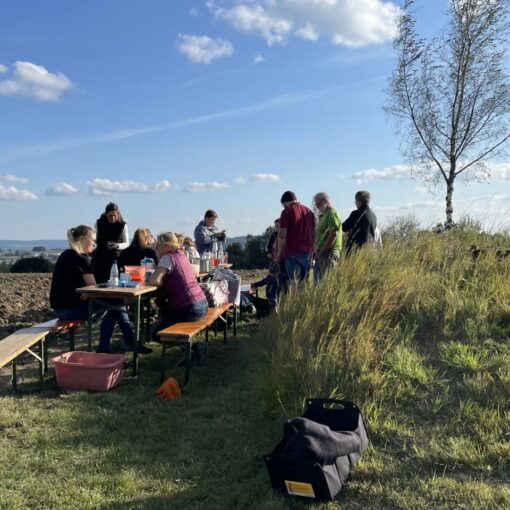 Kinder und Eltern sitzen zusammen auf Biergarnituren auf dem Kartoffelfeld und machen Pause.
