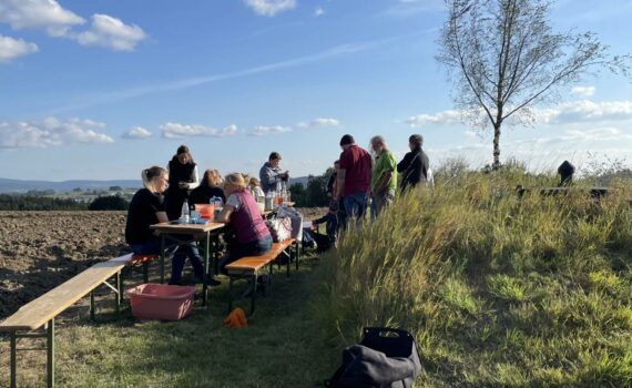 Kinder und Eltern sitzen zusammen auf Biergarnituren auf dem Kartoffelfeld und machen Pause.