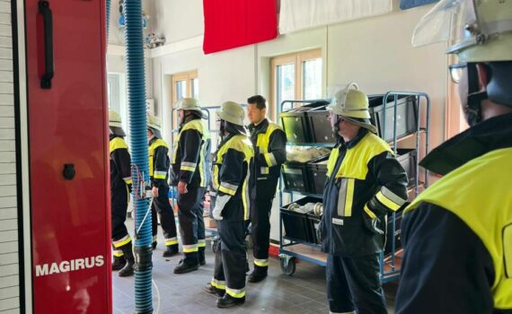 Die Feuerwehrmänner und -frauen stehen im Gerätehaus und warten auf die Übung.